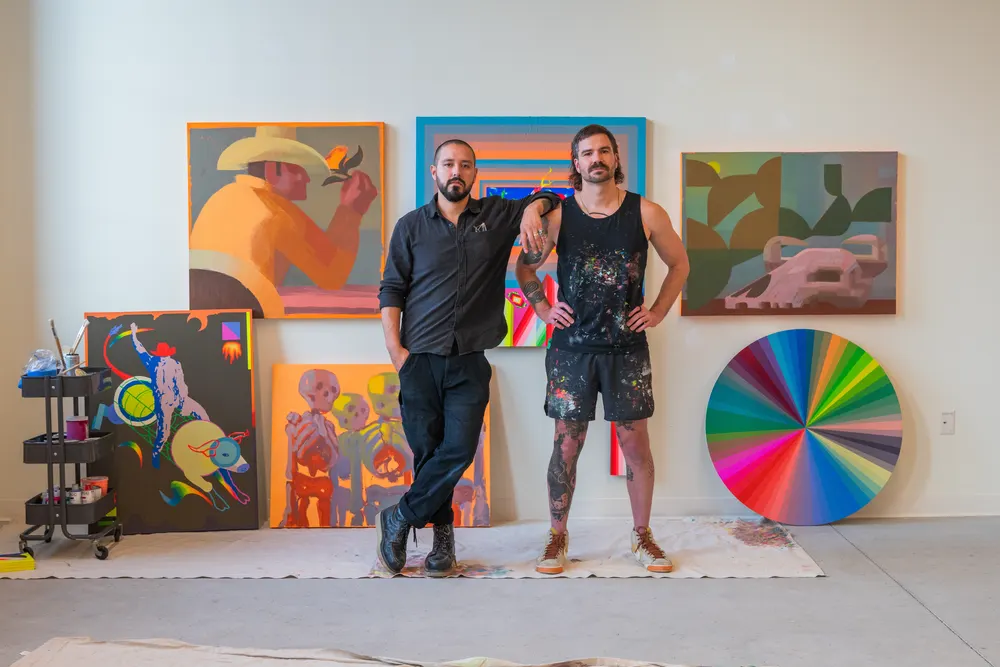 Two artists standing among their paintings in a studio