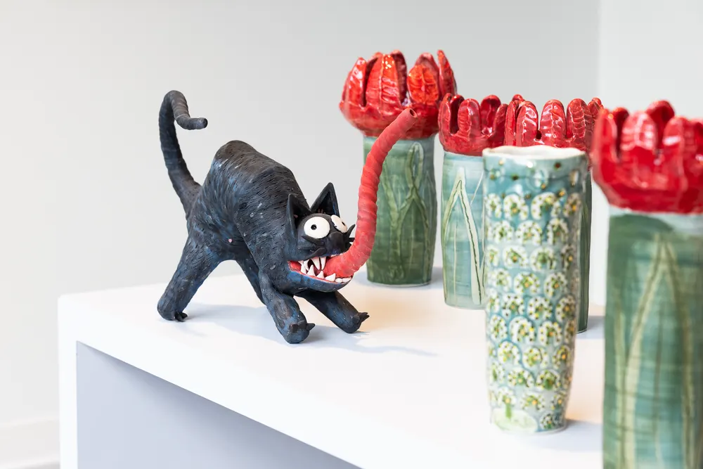 Ceramic sculptures of a black cat and red-topped vases on a plinth