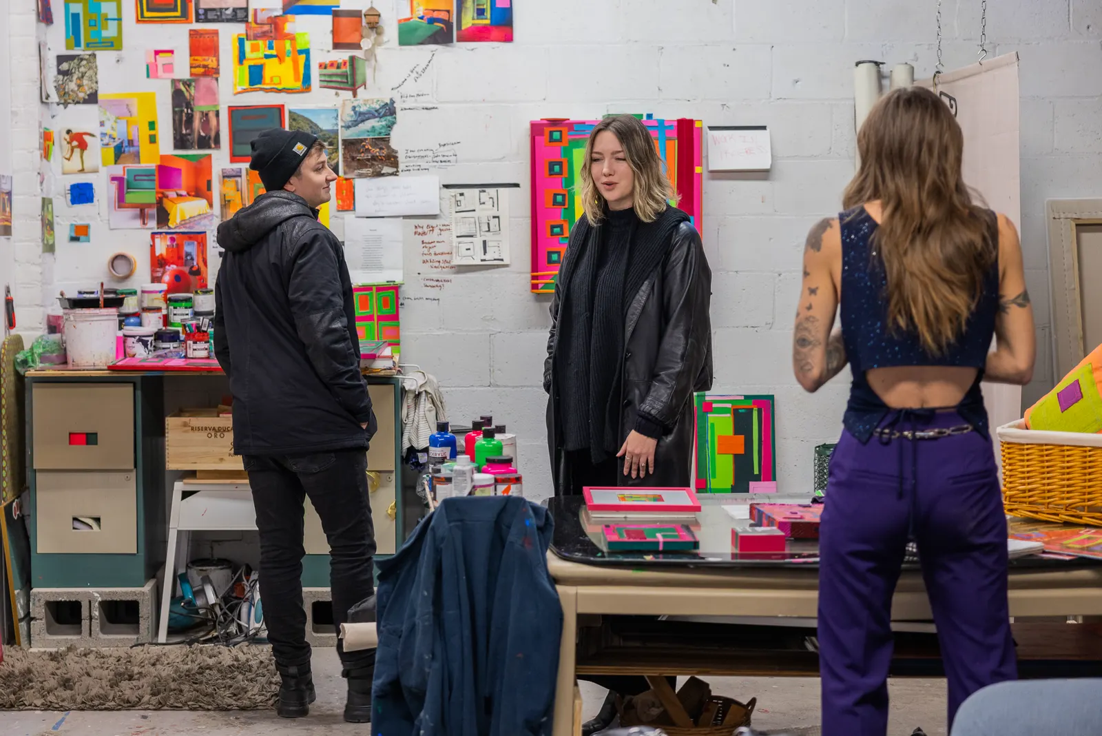 Three people talking in an artist's studio filled with colourful work