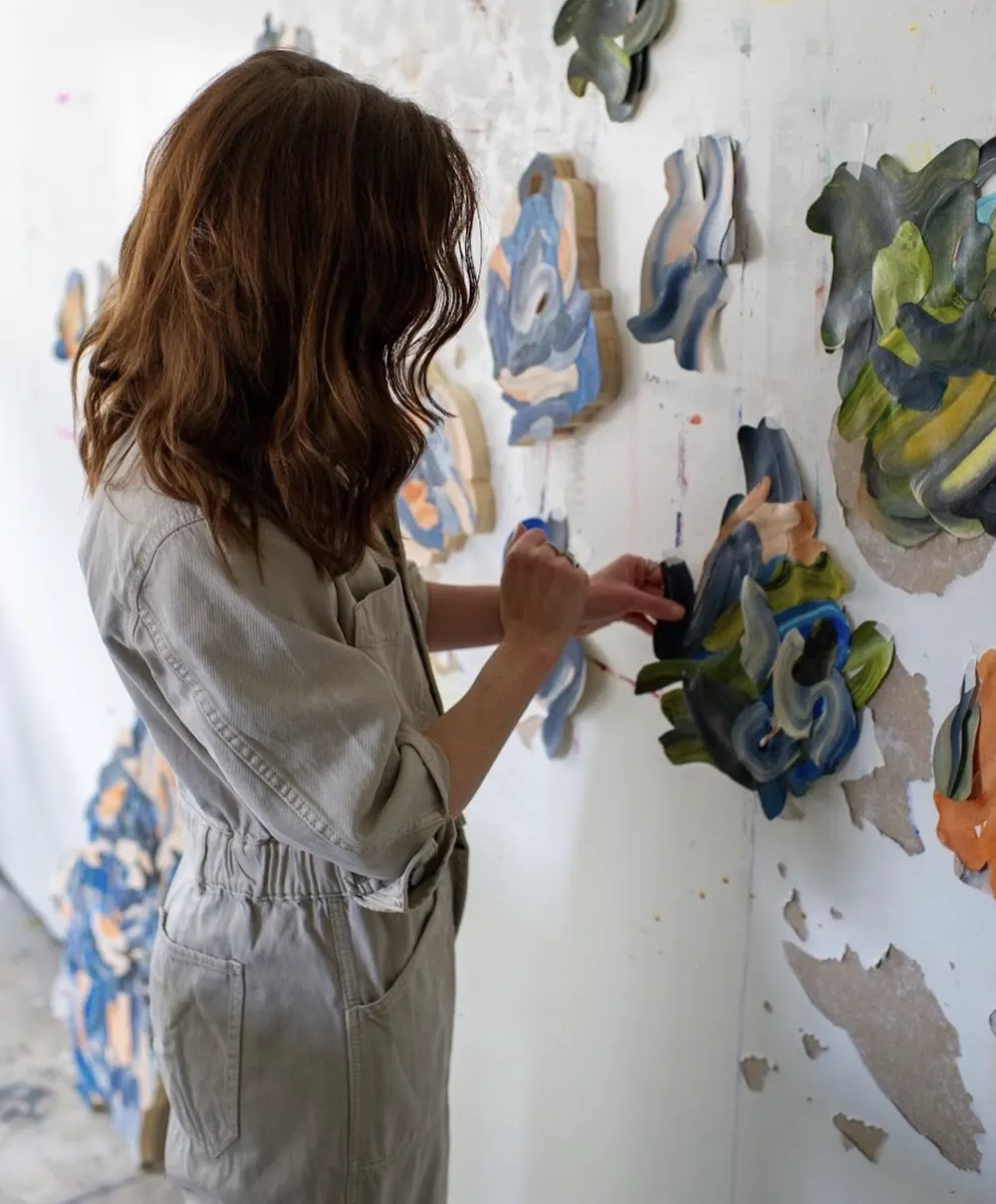 An artist installing sculptural pieces on a studio wall