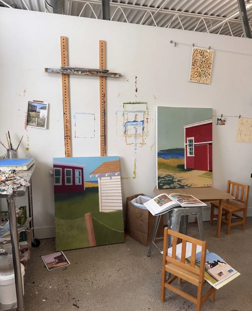 A studio with paintings of red barns on the walls and easels
