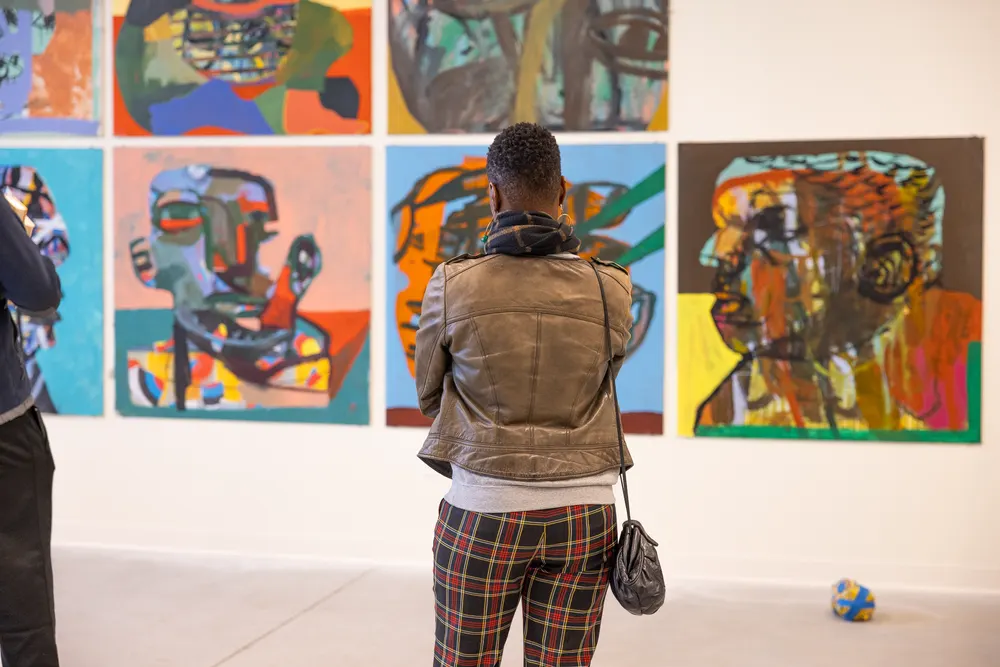 A visitor looking at a wall of colourful portrait paintings